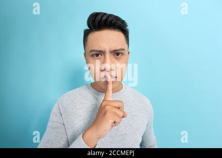Young handsome man asking for silence and quiet, gesturing with finger in front of mouth, saying shh or keeping a secret Stock Photo