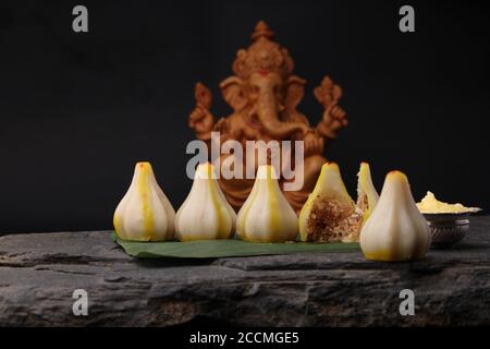 Modak- a traditional dish made on Ganpati festival in India. served with clarified butter. Ganesh idol at background Stock Photo