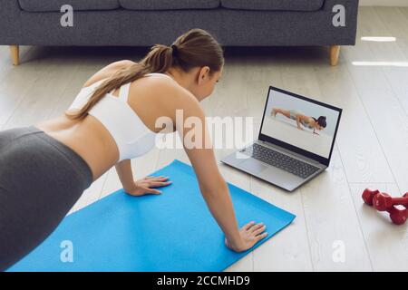 Fitness online. Young fit girl at home on the floor doing exercises, stretching warm-up and uses a video fitness lesson on the Internet. Stock Photo