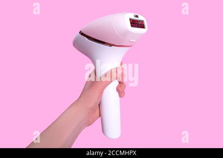 The girl holds a photoepilator in her hand. A device for removing unwanted hair isolated on pink.