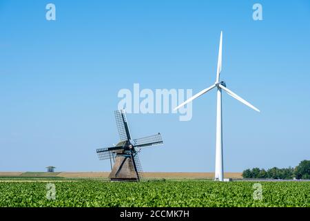 Big contrast of an old traditional windmill next to a modern wind turbine under a clear blue sky Stock Photo