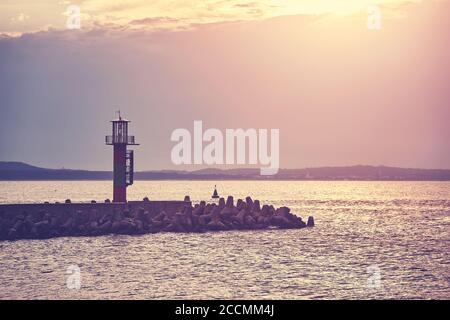 Pier with lighthouse at sunset, color toning applied, Swinoujscie, Poland. Stock Photo