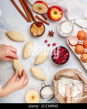 woman makes homemade pies with apples, cranberries and cinnamon on a marble table. The concept of home baking. Top view, selective focus Stock Photo