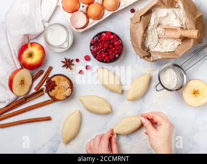 woman makes homemade pies with apples, cranberries and cinnamon on a marble table. The concept of home baking. Top view, selective focus Stock Photo