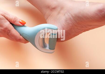 Close-up of care and cleansing of the woman feet from rough, flaky skin. An electric roller file in a woman's hand grinds foot heel at home, against t Stock Photo