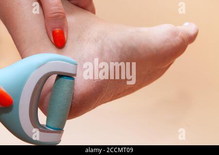 Close-up of care and cleansing of the woman feet from rough, flaky skin. An electric roller file in a woman's hand grinds foot heel at home, against t Stock Photo
