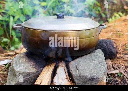 An aluminium pot on a wood fire restin gon two stones on the ground Stock Photo