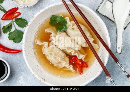 Fresh hot soup with dumplings (gedza, wontons) of chicken, pork or shrimp with soy sauce, chili pepper, cilantro and sesame seed in a white plate Stock Photo