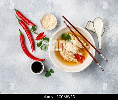 Fresh hot soup with dumplings (gedza, wontons) of chicken, pork or shrimp with soy sauce, chili pepper, cilantro and sesame seed in a white plate Stock Photo