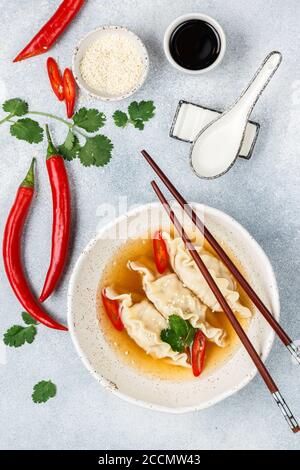 Fresh hot soup with dumplings (gedza, wontons) of chicken, pork or shrimp with soy sauce, chili pepper, cilantro and sesame seed in a white plate Stock Photo