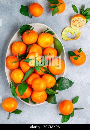 Fresh citrus mandarin oranges fruit (tangerines, clementines,) with leaves in a light dish on a gray stone or concrete background. Selective focus, to Stock Photo