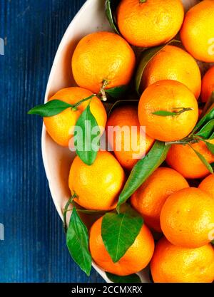 Fresh organic citrus mandarin oranges fruit (tangerines, clementines) with leaves in a light dish on a blue background close-up. Selective focus, top Stock Photo