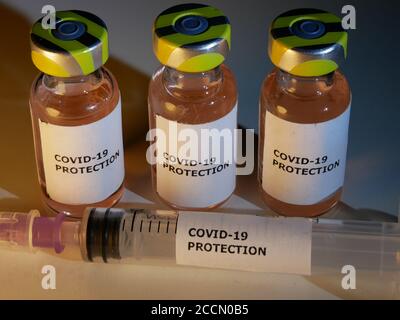Vials of vaccine against covid-19 with injection needle and protection against coronavirus label in close up Stock Photo