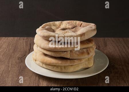 various pita breads stacked on a white plate on a wooden board with black background Stock Photo