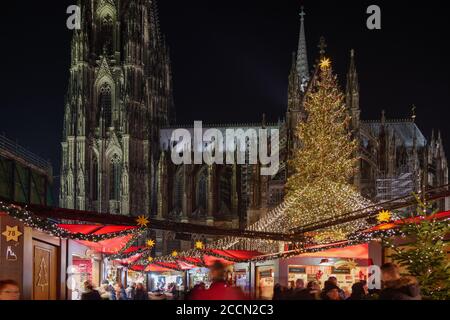 Night scenery, Weihnachtsmarkt, Christmas Market in Köln, with various decorated illuminate stalls in front of Christmas tree and Cologne Cathedral. Stock Photo