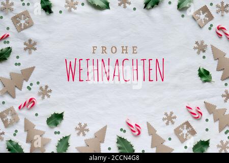 Text Frohe Weihnachten means Merry Christmas in German. Eco friendly decor from craft paper, red white candy canes and natural green holly leaves. Xma Stock Photo