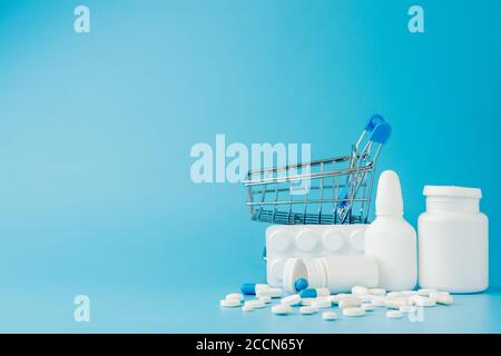 scattered variety pills, drugs, spay, bottles, thermometer, syringe and empty shopping trolley cart on blue background. pharmacy shopping concept Stock Photo