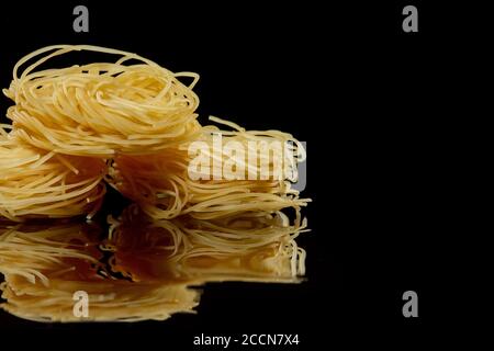 Dry, raw egg pasta capelli , isolated on black background. Cooking concept. Top view with copy space. Stock Photo