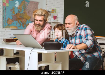 Serious older grandfather using laptop. Generation of people and stages of growing up. Little boy enjoy time with elderly Grandfather and father. Stock Photo