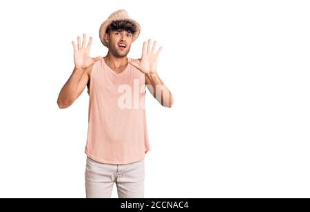 Young hispanic man wearing summer hat afraid and terrified with fear expression stop gesture with hands, shouting in shock. panic concept. Stock Photo