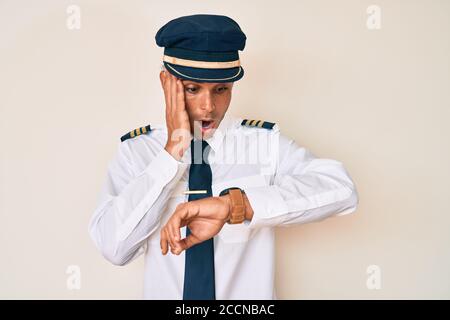 Young hispanic man wearing airplane pilot uniform looking at the watch time worried, afraid of getting late Stock Photo