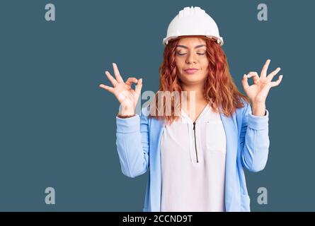 Young latin woman wearing architect hardhat relax and smiling with eyes closed doing meditation gesture with fingers. yoga concept. Stock Photo