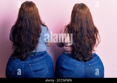 Young plus size twins wearing casual clothes standing backwards looking away with crossed arms Stock Photo
