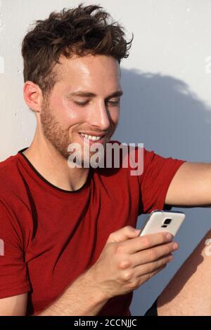 Mobile phone man texting sms on smartphone app. Smiling young urban sporty guy using cellphone in urban outdoor city summer day or after run workout Stock Photo