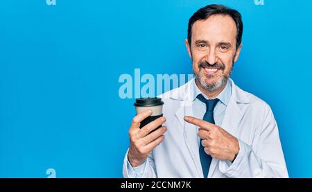 Middle age handsome doctor man wearing coat drinking cup of takeaway coffee smiling happy pointing with hand and finger Stock Photo