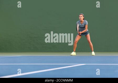 Tennis player woman standing ready to play waiting to receive serve. Outdoor fitness instructor focused playing on hard court on green background Stock Photo
