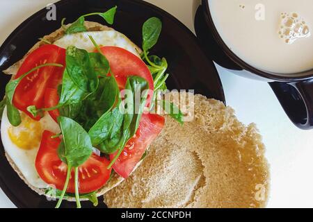 home breakfast meal - fried eggs with tomato and fresh spinach on pita, tea with milk Stock Photo