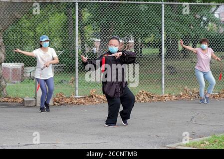 An Asian American man wearing a face mask leads a small Tai Chi class holding a sword. In a park in Queens, New York City. Stock Photo