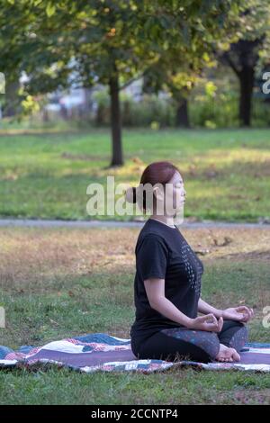 A Chinese American woman sits in the lotus position at a yoga class in a park in Queens, New York Stock Photo