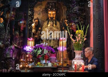 Altar inside a temple. Man arranging religious offerings and candles to a bearded sacred statue. Neon lights. Ngoc Hoang Pagoda, Ho Chi Minh, Vietnam Stock Photo