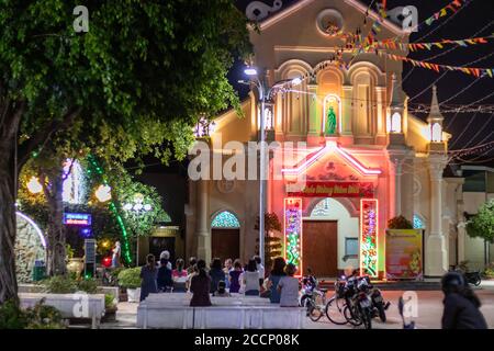 Catholic cathedral at night. People praying, mass celebration outside the building. Neon lights. Concrete benches. Scooters. Can Tho, Vietnam Stock Photo