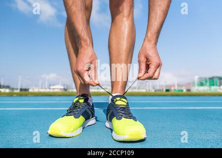 Runner tying running shoes laces on run tracks lanes in stadium getting ready for race competition outdoor on track and field. Sport athlete man Stock Photo