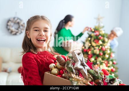 Merry Christmas and Happy Holidays!  Grandmother, mother and child decorating the tree in room. Loving family indoors. Stock Photo