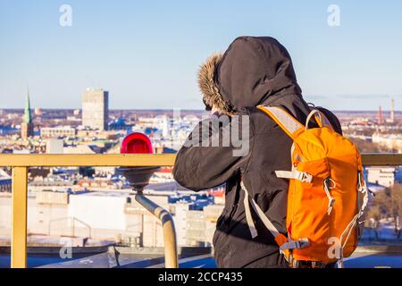 Photographer with big bag taking picture landmark the ancient european city from a high view point. Latvian Academy of Sciences. Sunny winter day Stock Photo