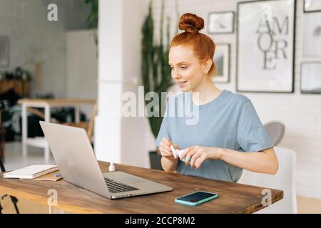 Cute young redhead businesswoman is wiping laptop computer with sanitizer before starting work  Stock Photo