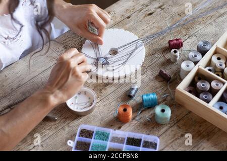 Top angle view of a woman work from home making hand made micro macrame jewel with colored spools of thread - Reinvent your life with independent job Stock Photo
