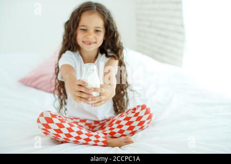 The baby is drinking milk. A little girl at home on the bed drinks yogurt.  Stock Photo