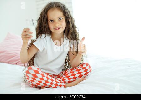 The baby is drinking milk. A little girl at home on the bed drinks yogurt.  Stock Photo