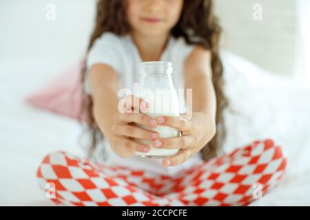 The baby is drinking milk. A little girl at home on the bed drinks yogurt.  Stock Photo