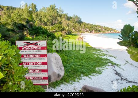 Warning sign post of strong current at the beach of Petite Anse, La Digue island, Seychelles Stock Photo