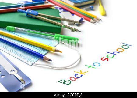 Colorful school supplies and medical protection face mask against coronavirus and covid 19 infection, new normal concept, text Back to school, white b Stock Photo