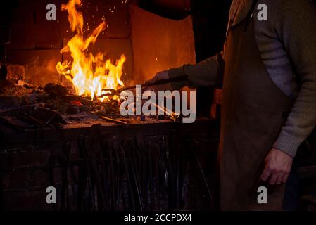 Blacksmith working with open fire in furnace. The blacksmith forging hot iron in workshop Stock Photo