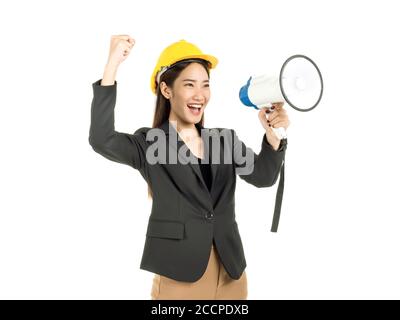 Young Asian woman engineer wearing suit and yellow safety helmet holding a megaphone and raise hand with success smiling isolated on white background. Stock Photo