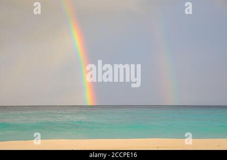 Colourful two rainbows over the sea with waves and sandy beach in Petite Anse, La Digue Island, Indian Ocean, Seychelles Stock Photo