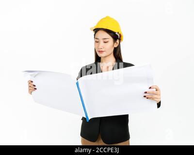 Young Asian businesswoman wearing black suit and yellow safety helmet checking project engineering paper plans in hands. Portrait of female engineer l Stock Photo