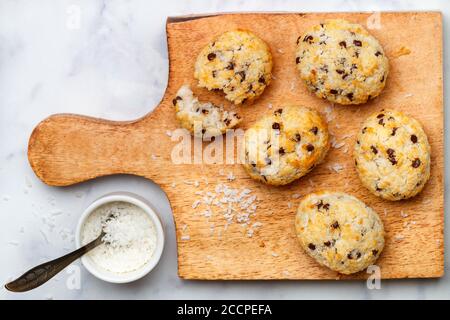 Freshly baked homemade cookies (biscuits) with coconut and chocolate drops on a wooden Board on a marble background. Delicious crispy dessert for Brea Stock Photo